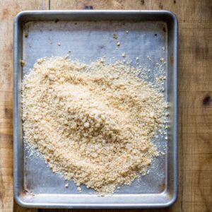 "Homemade sourdough breadcrumbs in a rustic bowl with slices of sourdough bread on a wooden board.