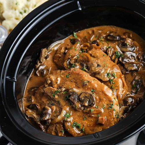 “Juicy slow-cooked pork chops in a Crock Pot, garnished with herbs”