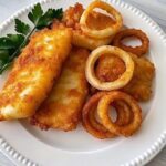 Golden crispy cod fillets with crunchy golden onion rings on a platter