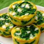Spinach and feta egg muffins freshly baked in a muffin tin, golden brown on top with visible spinach and feta pieces.