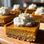 Pumpkin pie bars topped with whipped cream on a white plate